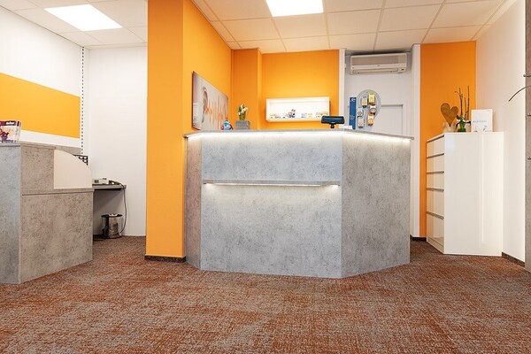 Moderner Empfangsbereich mit orangefarbenen Wänden und beleuchtetem Tresen in Praxis.